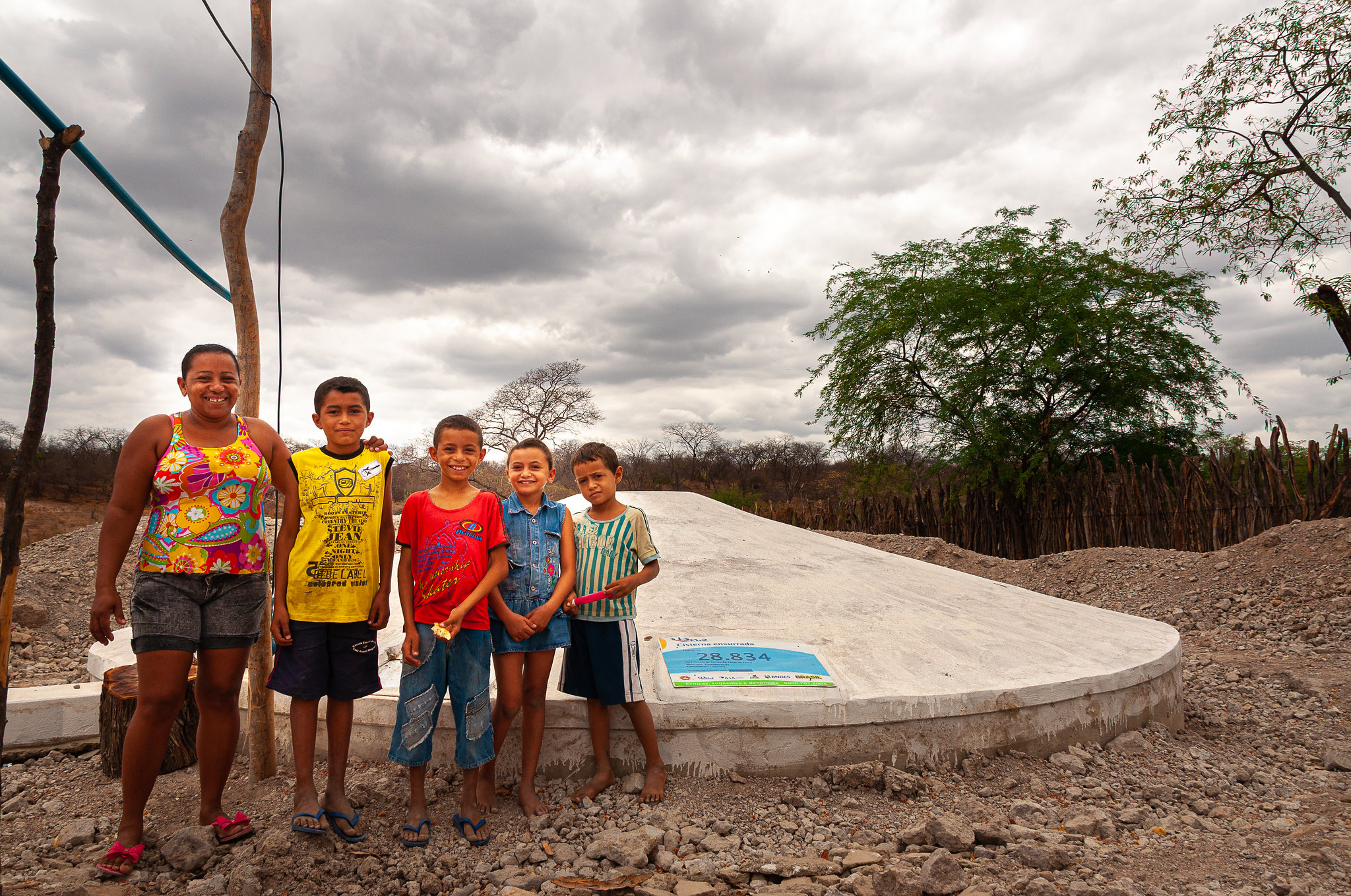 Mulher com quatro crianças sorridentes pousam para foto na frente de sua cisterna de segunda água.
