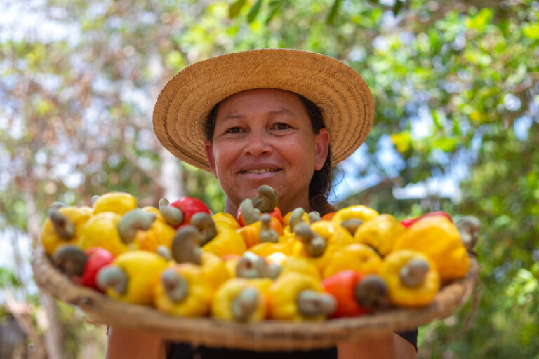 Agricultora posa para foto com um cesto de cajus nas mãos.