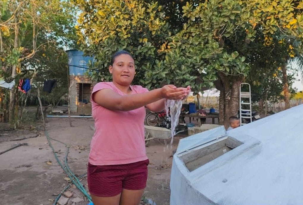 A agricultora Karoline segura água com as mãos ao lado de sua cisterna.