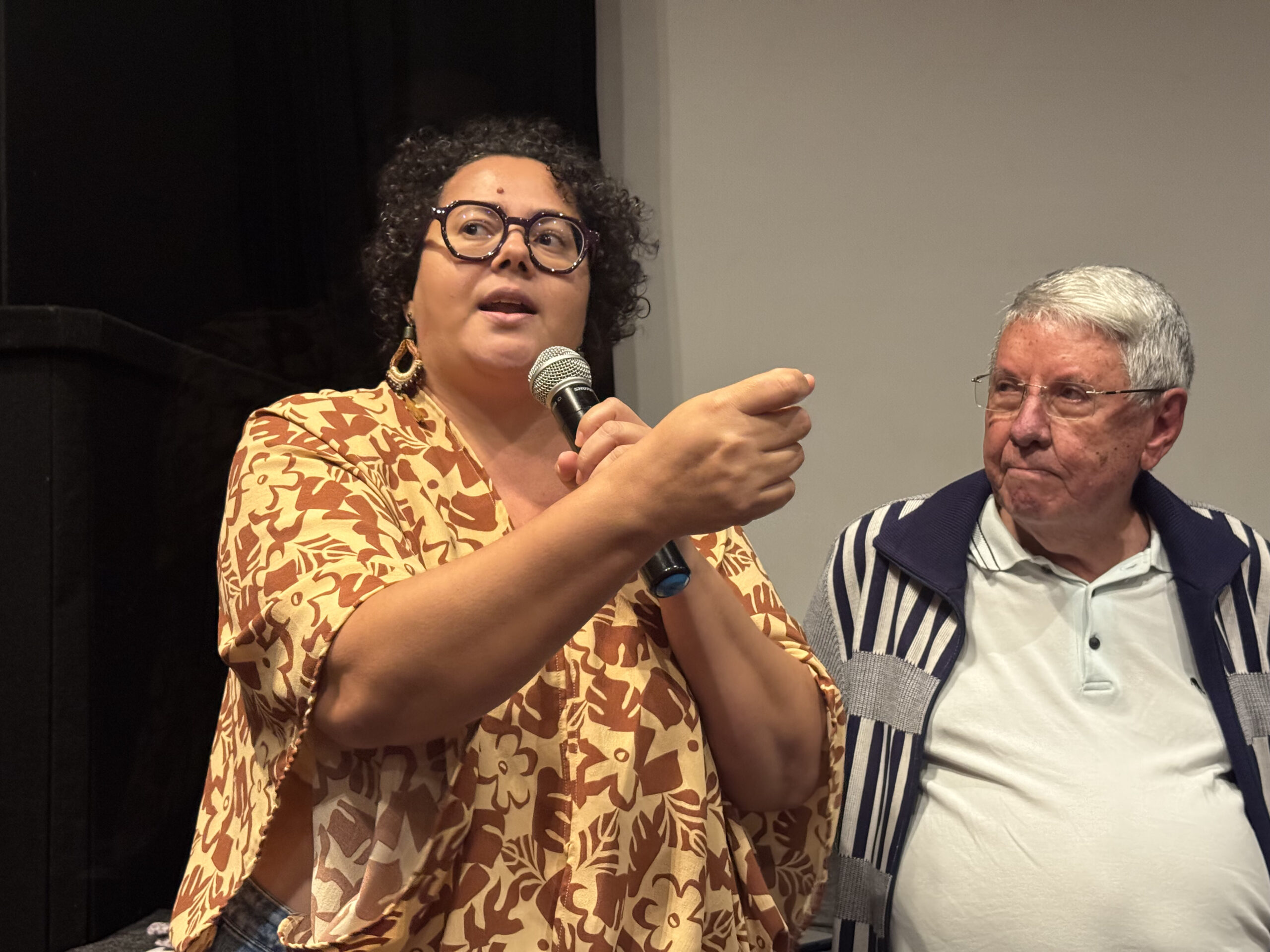 Uilma Queiroz, roteirista e diretora do filme O Bem Virá fala no cinema com microfone na mão.
