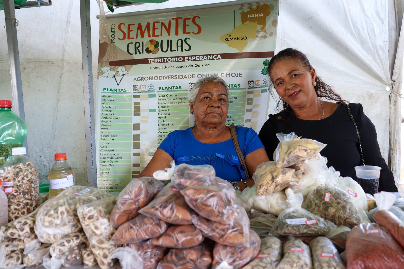 Duas agricultoras atrás de uma mesa com sementes crioulas.
