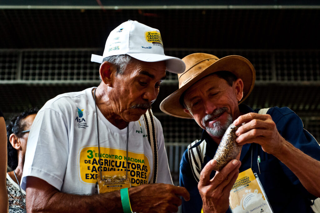 Na foto vemos dois agricultores conversando, um deles com a camisa do 3º Encontro Nacional de Agricultores e Agricultoras Experimentadores.
