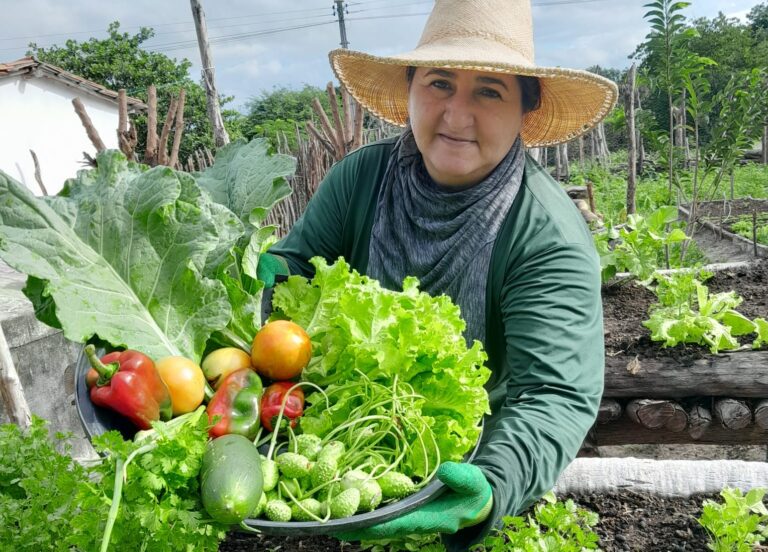 Agricultora de chapéu com verduras nas mãos.