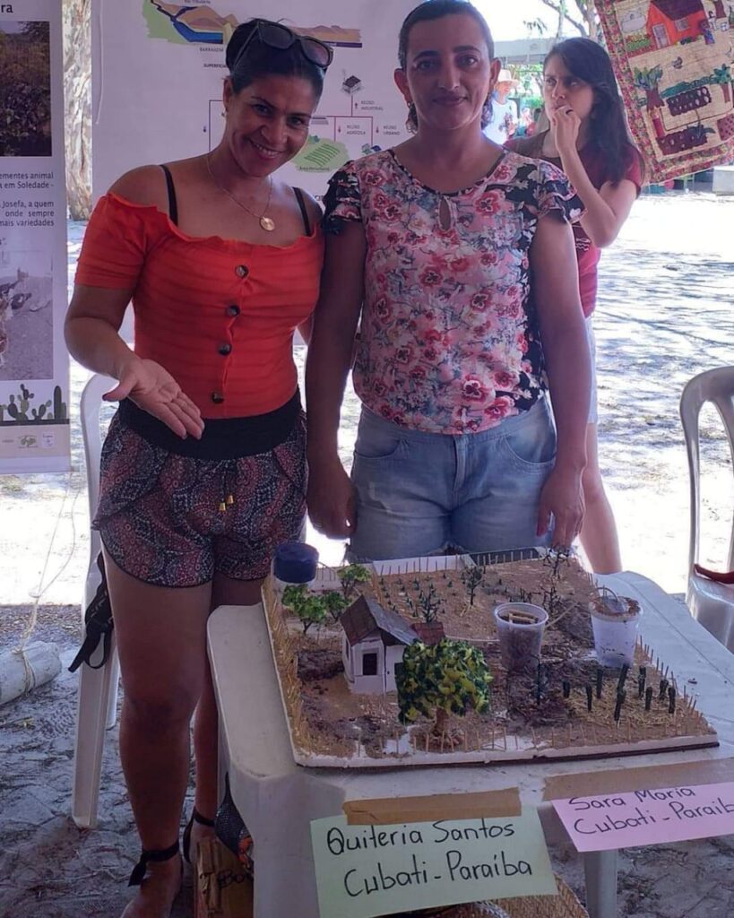 Na foto, duas mulheres mostram uma maquete com experimentos tecnológicos no semiárido.