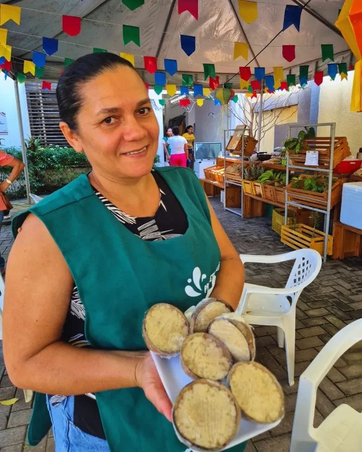 uma mulher em frente a sua barraca de feira mostrando os produtos disponíveis para feira produzidos com o que produz na roça
