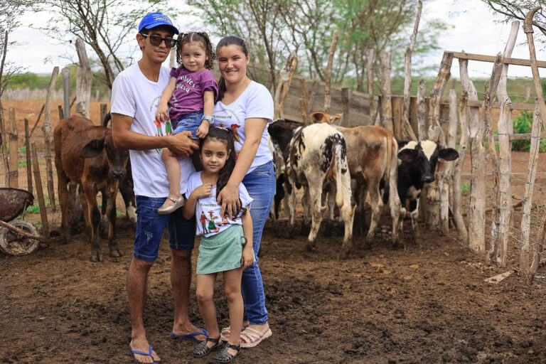 Família com pai, mãe e duas meninas junto a alguns animais no curral