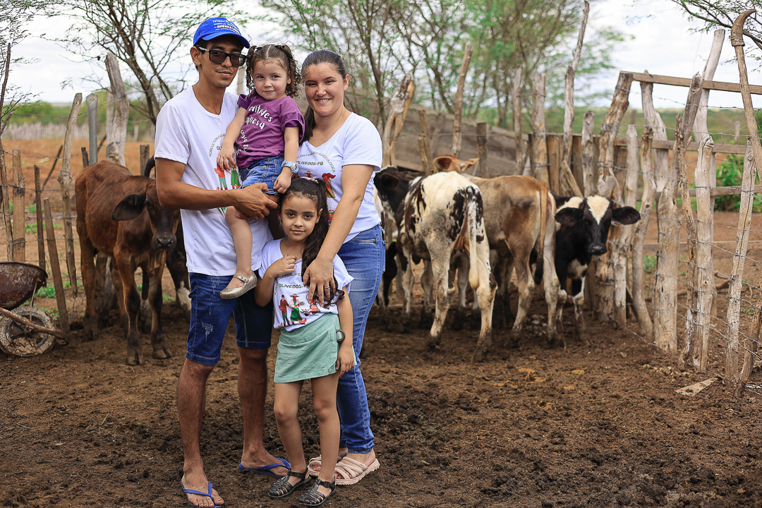 Família com pai, mãe e duas meninas junto a alguns animais no curral